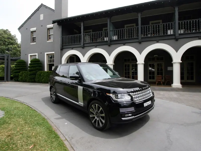Polished dark Range Rover Autobiography parked on a single-track road beside a stone distillery wall